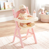 Baby doll sits in a pink high chair with a bowl and a baby bottle on the feeding tray.
