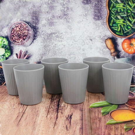 A set of six grey cups on a wooden table with vegetable background.