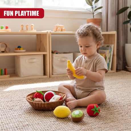 A toddler sits on a rug holding a yellow fabric banana from The Magic Toy Shop's Fabric Fruit Basket Toy Set, surrounded by