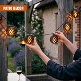 Hands hang rattan woven solar lights strung across a dark wooden patio structure.