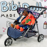 A blue twin doll stroller holds two seated dolls dressed in contrasting colored outfits.
