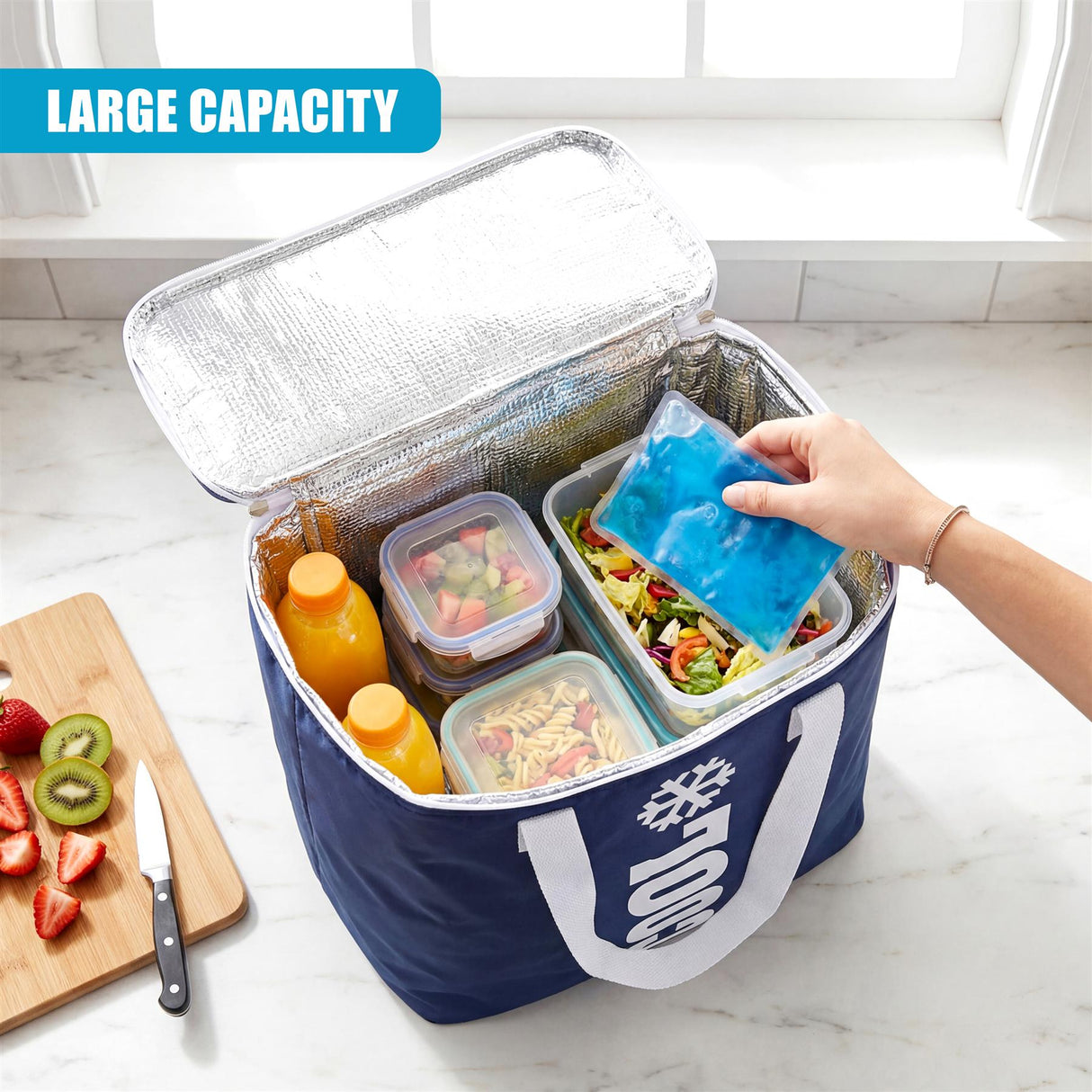 Open blue cooler bag holds prepared food, juice, and a cold pack; visible cutting board has fruit.