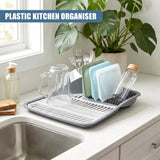 Gray plastic dish drying rack holds glassware, utensils, and bottles on a kitchen counter.