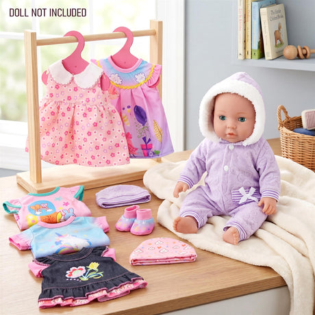 Doll clothes including two dresses, a doll in purple outfit, and various folded accessories on wood.