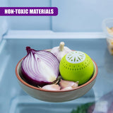 A bowl contains an onion half, garlic cloves, and three perforated bright green spherical deodoriser objects.