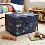 A large navy blue space-themed storage box with a lid, decorated with rockets, planets and stars, sits on a cream rug