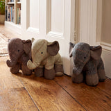 Three stuffed elephants decorated with different tartan patterns sit on a wooden floor.
