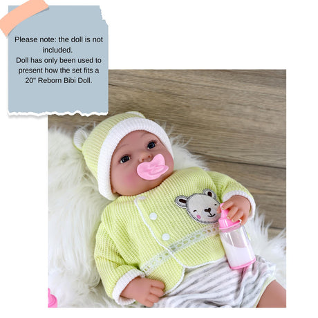 Reborn doll wearing a light green outfit with a bear appliqué and holding a feeding bottle.