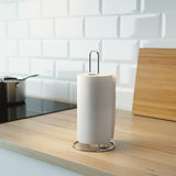 Two images of a sleek, chrome kitchen roll stand with a paper towel roll on top. It's placed on a counter next to a stove and a cutting board. - UKBuyZone