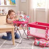Pink baby cot, high chair, small wooden table, and patterned travel bag displayed in a staged child's room.