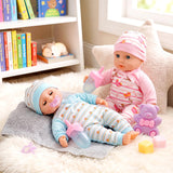 Two baby dolls dressed in pajamas, resting on a gray cloth with bottles and toys.