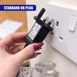 A hand holds a black battery eliminator adapter with a standard UK plug inserted into a white wall socket