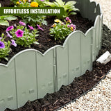 A curved, green metal garden edging fence separates a mulched flower bed filled with blooming plants.