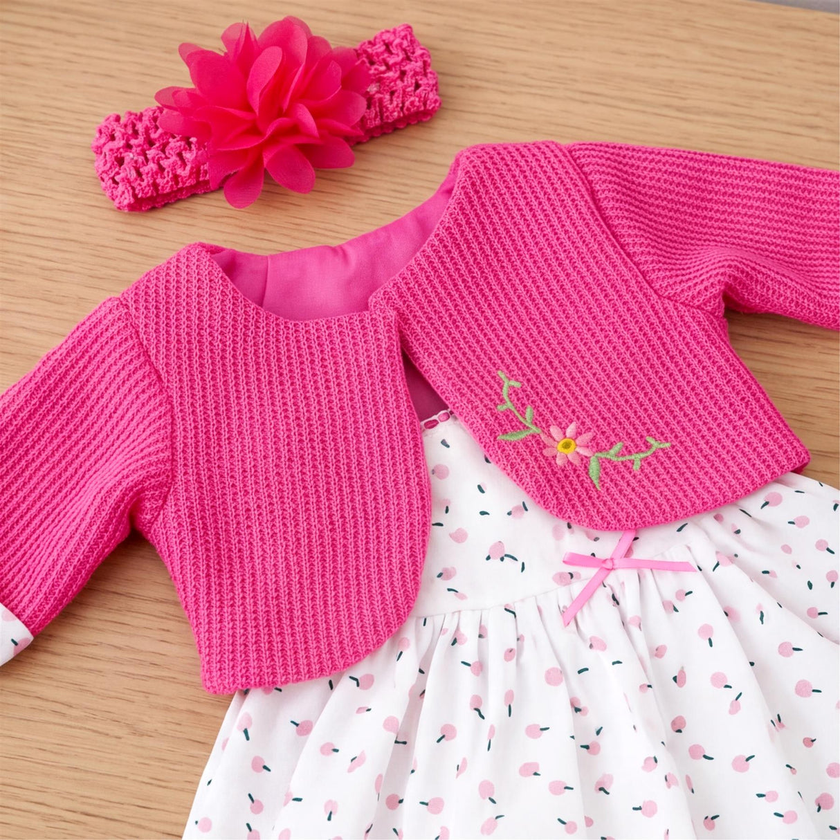 Pink knitted doll tops, a floral headband, and white polka dot dress set are displayed.