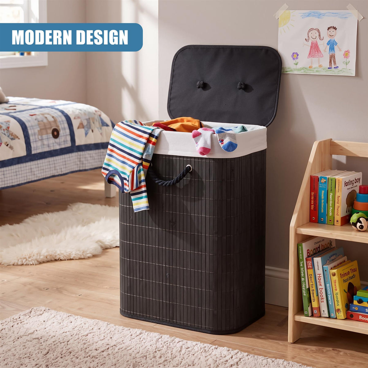 A black bamboo laundry hamper with a lid and rope handles, filled with clothes, sits on a wooden floor next to a bookshelf