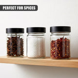 Three clear glass spice jars on a wood shelf, holding visible spices like star anise, white powder, and red blends.