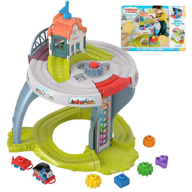 The toy table features train tracks, a station house, a small engine, and various colored geometric blocks.