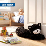A black, plush cat draft stopper rests on a light wooden floor near a white door.