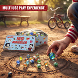 Hand reaching into a tin box filled with colorful glass marbles on dirt ground.