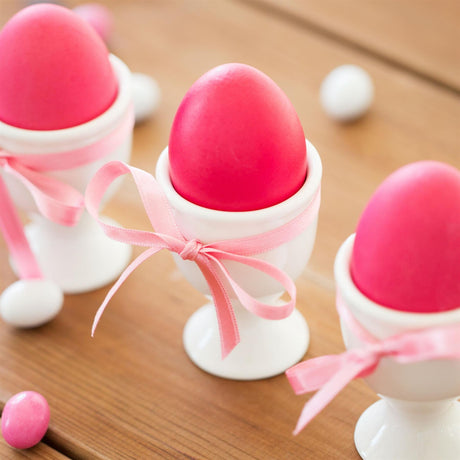 Three colorful egg cups with white spoons and pink bows on a wooden table.