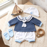 Miniature navy blue striped sailor outfit, hat, socks, and wooden boat accessory displayed together.