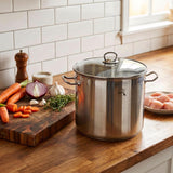 Stainless steel stockpot with a glass lid rests on a wooden counter near ingredients.