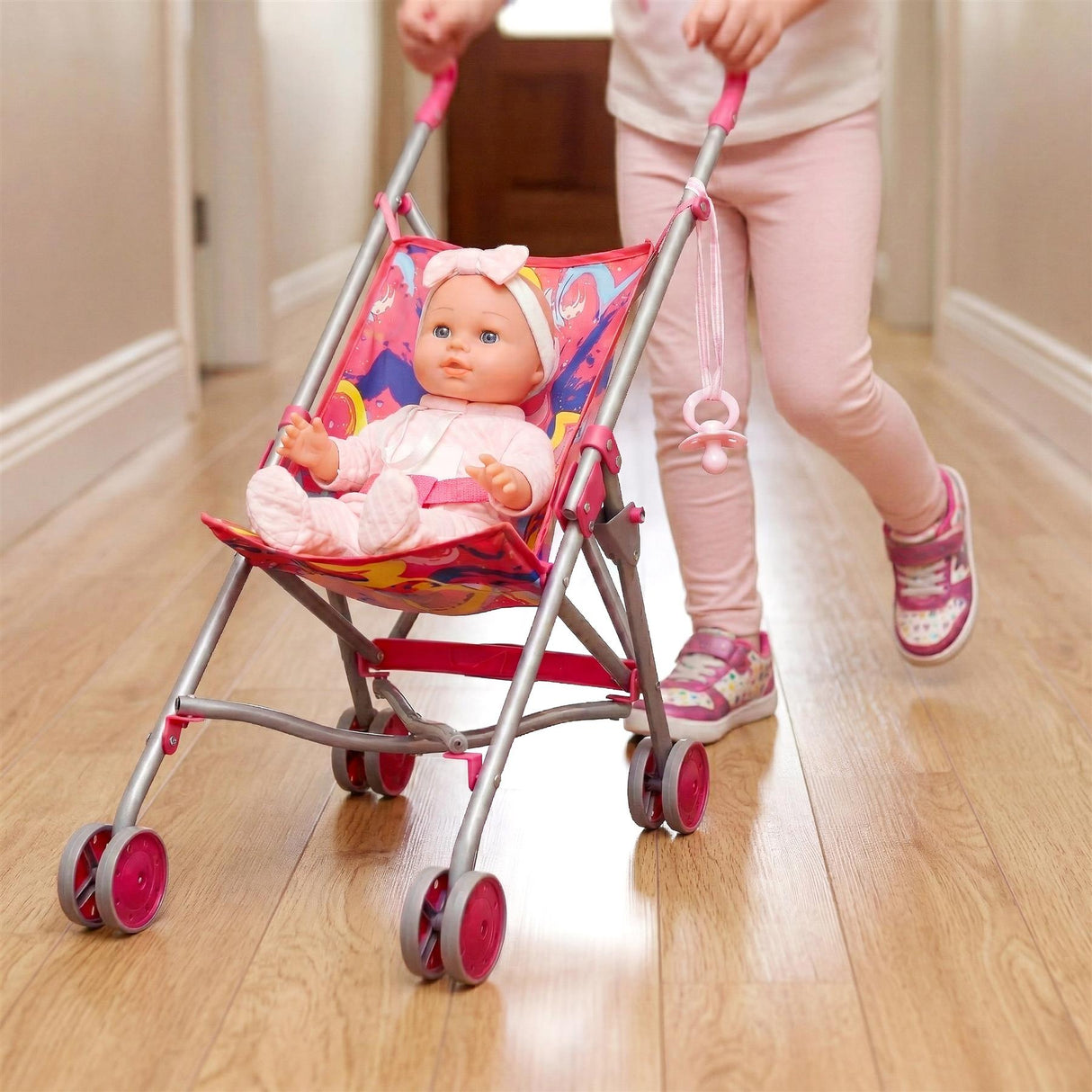 A pink baby buggy holding a doll, positioned on a hardwood floor, handled by a person.