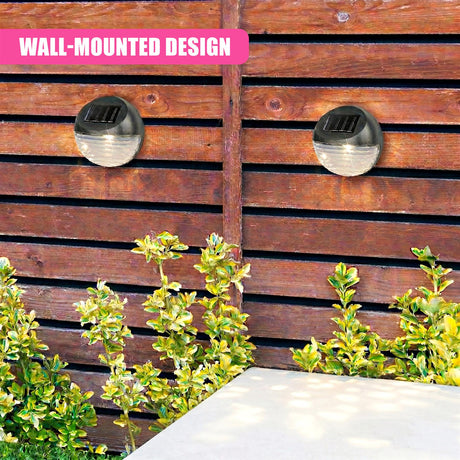 Two black, dome-shaped solar lights are mounted on a wooden fence next to green shrubs.
