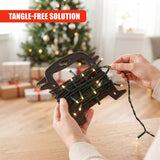 A person holds a black Christmas light reel storage device with illuminated lights, against a blurred background featuring a