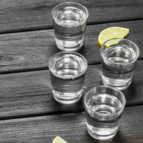 Four glasses of shot glasses on a table with limes.