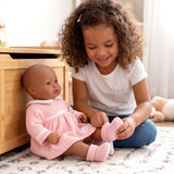 Young girl handles pink knitted socks while seated next to a doll in a matching pink dress.