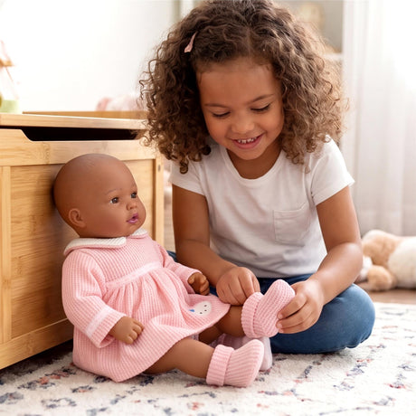 Young girl handles pink knitted socks while seated next to a doll in a matching pink dress.