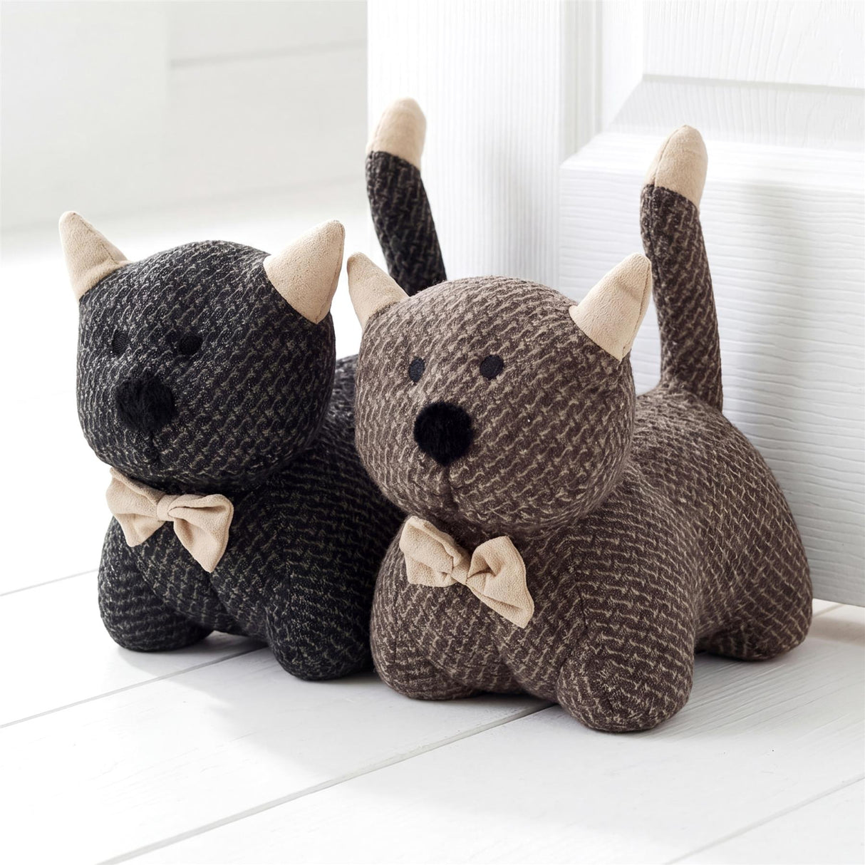 Grouping of three knitted stuffed animal figures in gray and brown, sitting on a white surface.