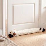 Plush cream draught excluder with black cat ends rests horizontally on a wooden floor.