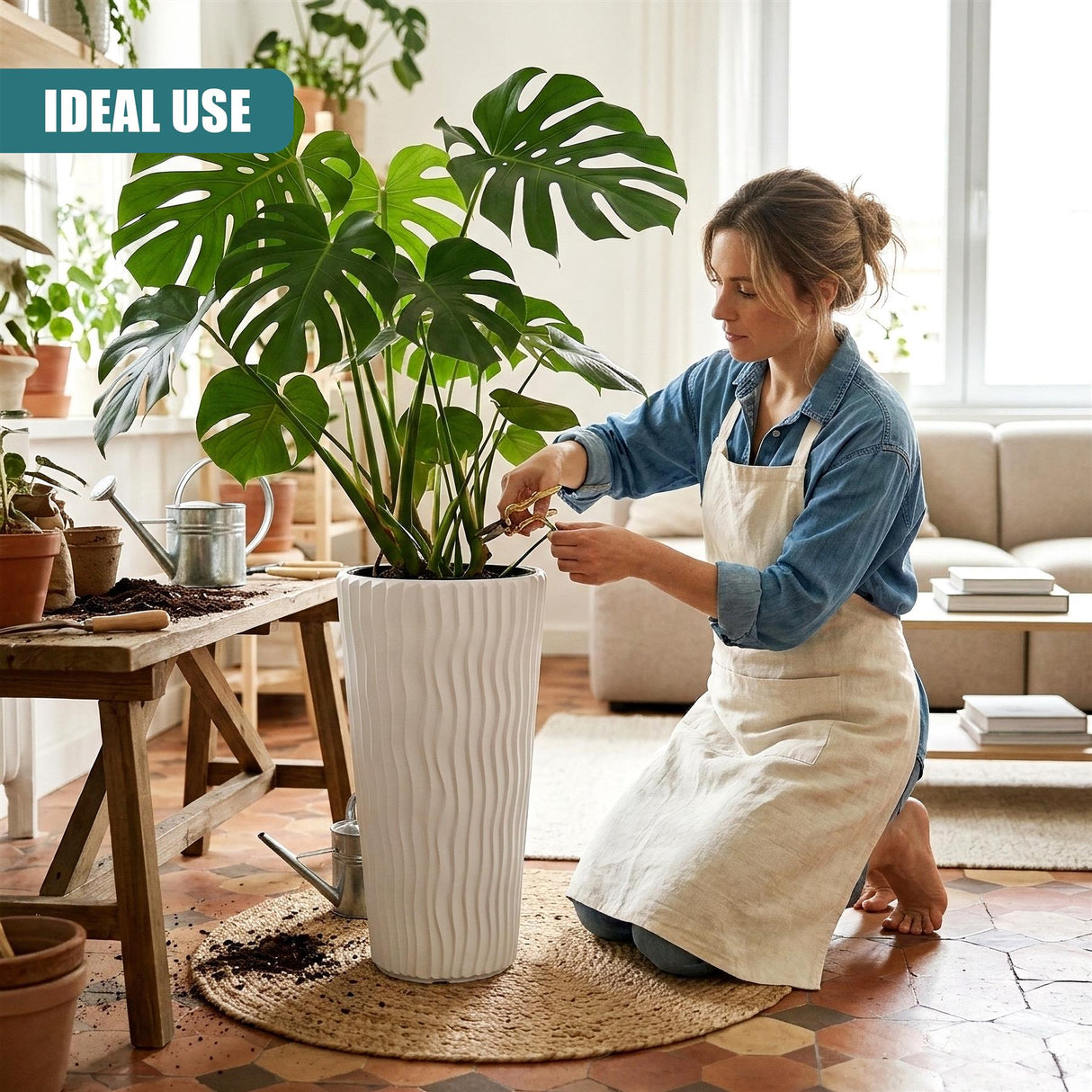 A woman in a denim apron tends to a large tropical plant growing in a tall, textured white pot.