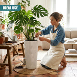 A woman in a denim apron tends to a large tropical plant growing in a tall, textured white pot.