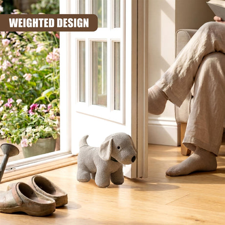 Knitted grey dog stopper rests on a wooden floor near a window with visible flowers.
