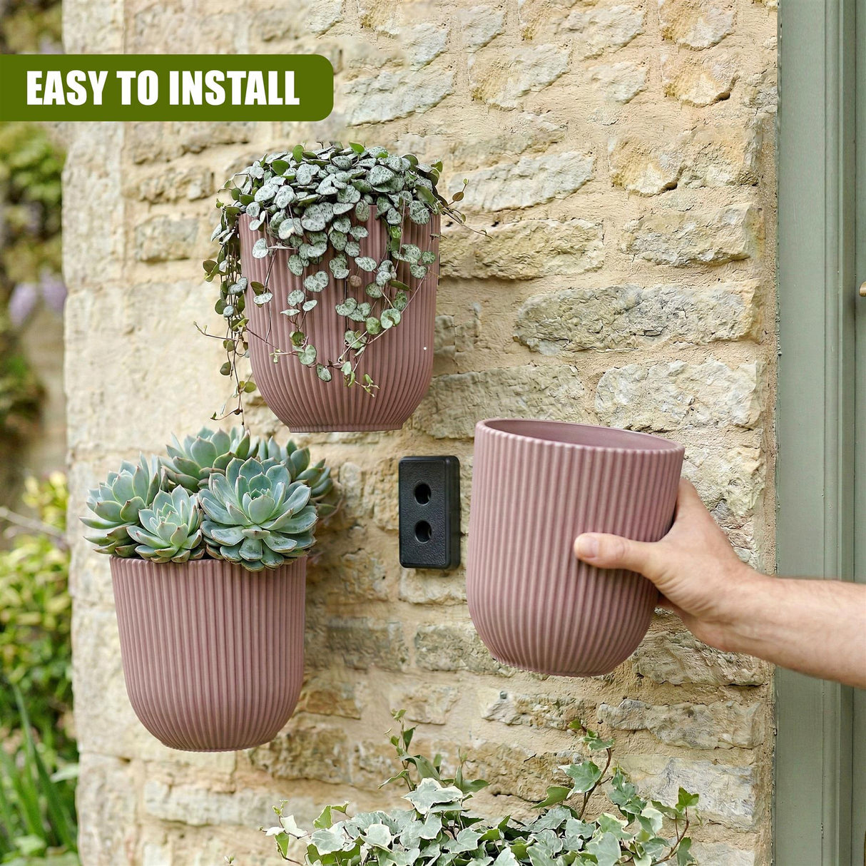 Ribbed terracotta planters holding succulents and foliage are mounted onto a stone wall.
