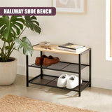 A black, two-tiered shoe bench holding shoes, books, and a bowl on the top surface.