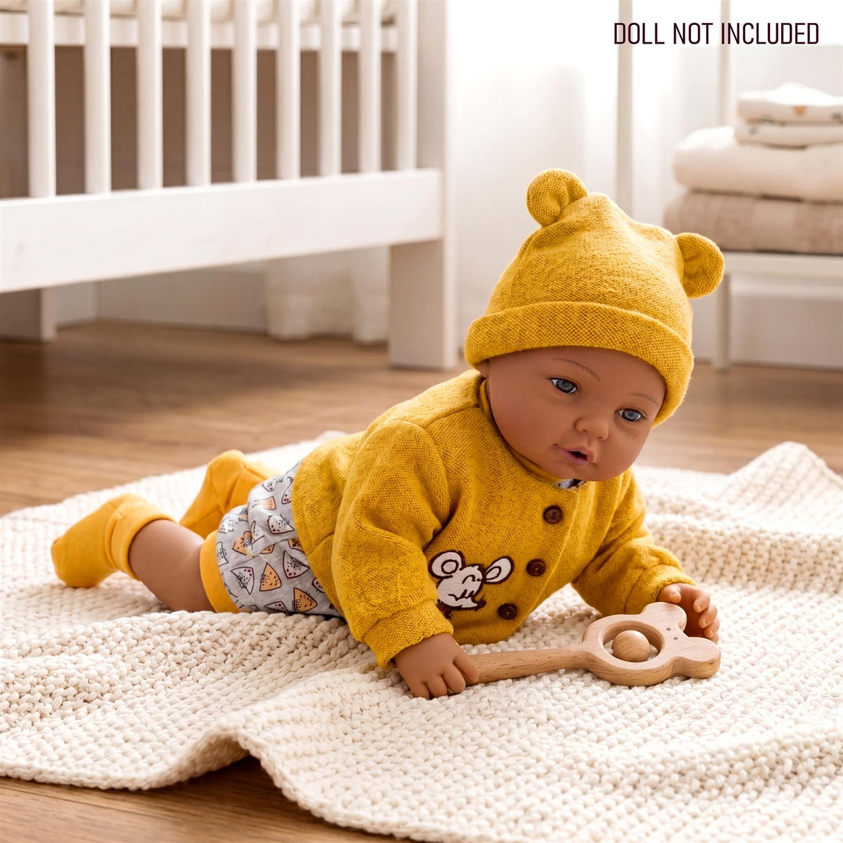 Doll dressed in yellow knit clothes, featuring a mouse design, holding a wooden rattle on a textured blanket.