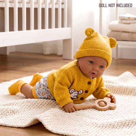 Doll dressed in yellow knit clothes, featuring a mouse design, holding a wooden rattle on a textured blanket.
