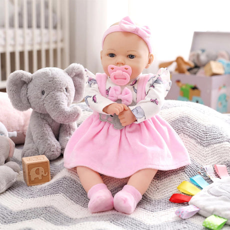 Doll in a pink dress and headband sits with a plush gray elephant toy on a patterned blanket.