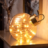 A large amber glass bauble with warm white LED lights and a metallic top loop sits on a shelf