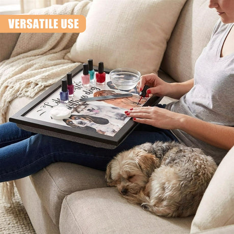 A woman sits on a couch, painting her nails while holding a tray with nail polish, a nail file, and a bowl of water. A small dog sleeps at her feet. The woman is surrounded by a cozy atmosphere, with a soft blanket and a few pillows. The tray has a fun design with a dog theme, featuring a dog's face and the phrase "I'd rather be with my dog." - UKBuyZone