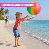 Boy on the beach plays with a large, rainbow-colored ball near the ocean and sandy shoreline.