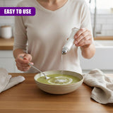 A hand sprinkles seasoning granules from a clear shaker bottle into a bowl of soup.