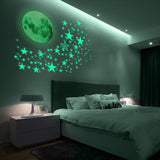 A bedroom with a bed, nightstand, and wall featuring a glow-in-the-dark moon and stars. The room is dark, with only a few lights on, and the glow-in-the-dark decorations are visible in the dark. - UKBuyZone