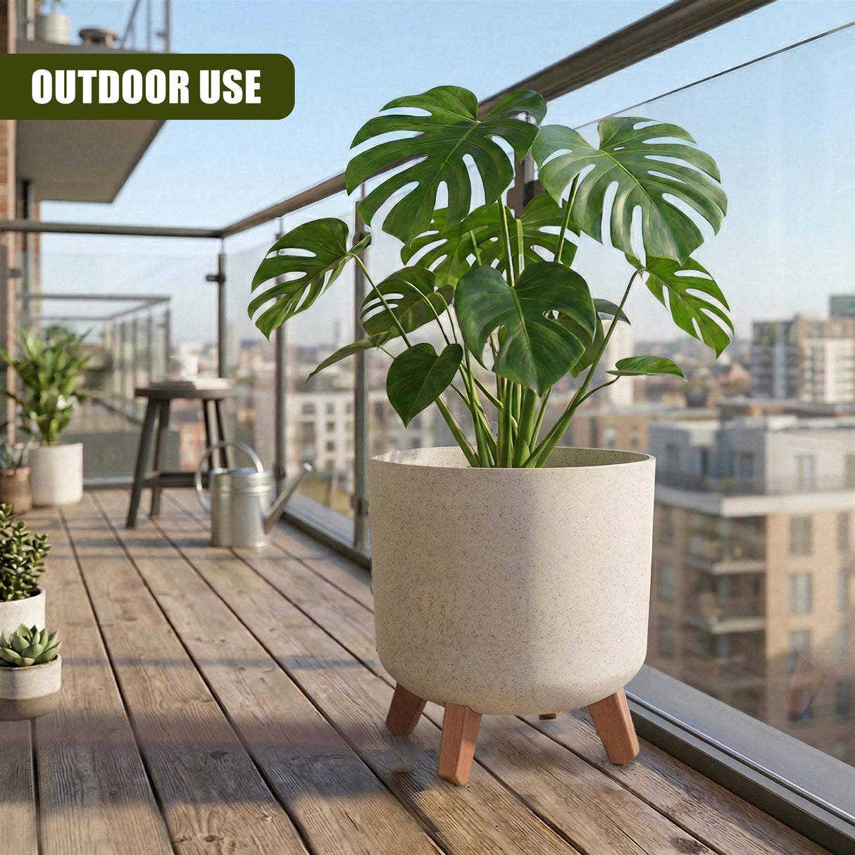 Large tropical plant in a neutral pot with wooden legs, displayed on a wooden outdoor deck surface.