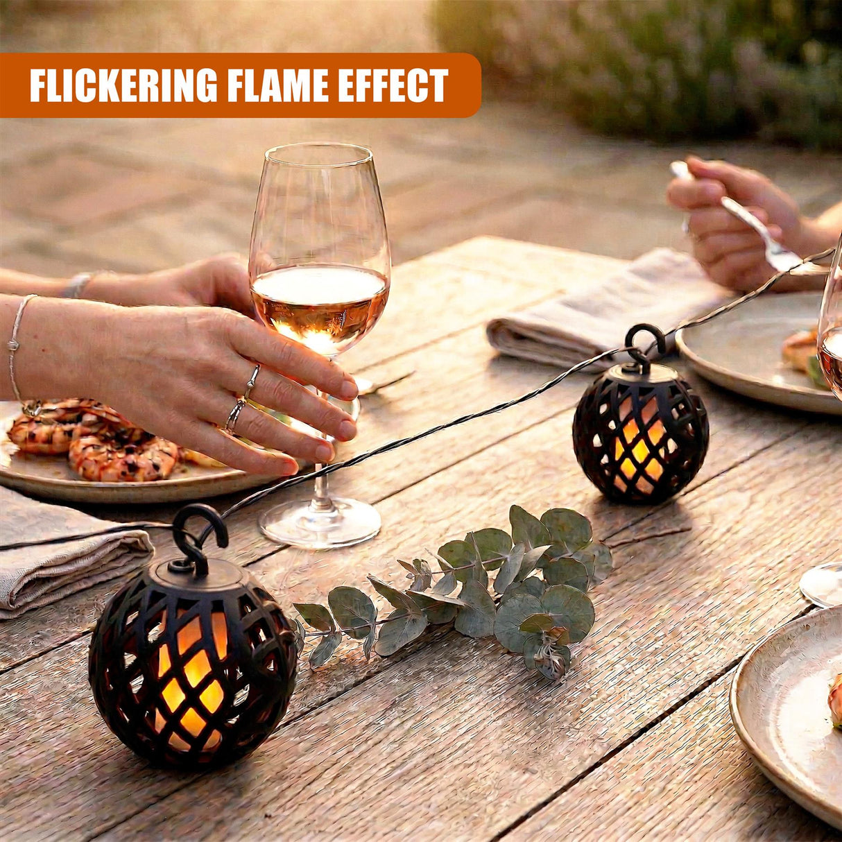 Black, patterned string lights draped over a rustic wooden table with wine and appetizers.