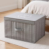 A gray fabric storage box with a heart pattern and "Neat and Tidy" on the lid, placed on a rug near a bed